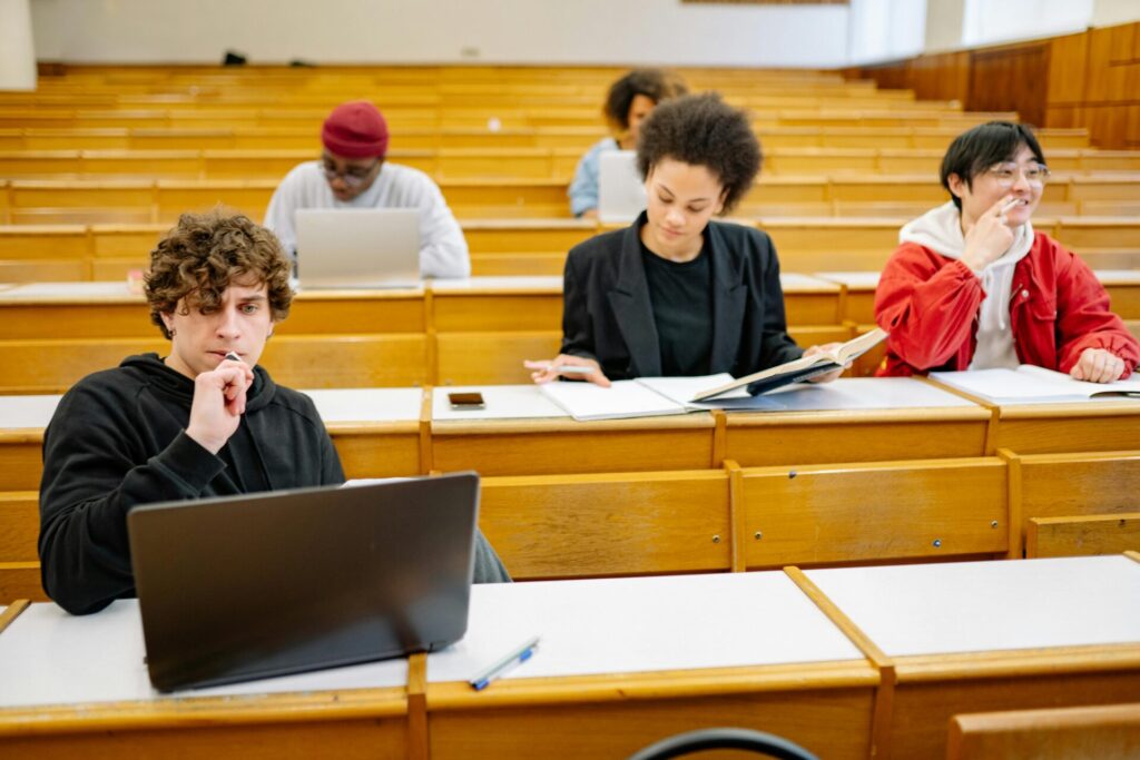 A diverse group of college students studying in a classroom setting with laptops and books.